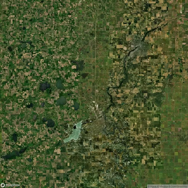 Aerial view of a landscape featuring a patchwork of fields, a winding river, scattered lakes, and a densely built area.