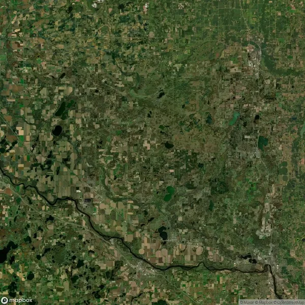 Aerial view of a landscape with a mix of agricultural fields, forests, and scattered lakes. A river flows across the bottom of the image.