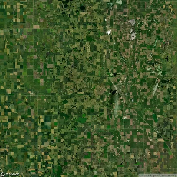 Aerial view of a patchwork agricultural landscape with irregularly shaped green and brown fields, intersected by roads and dotted with small bodies of water.