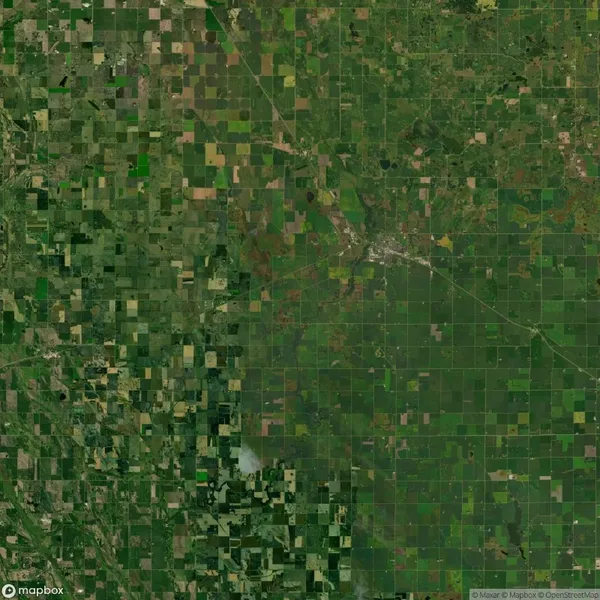 Aerial view of a vast expanse of farmland with a patchwork of fields in varying shades of green and brown, intersected by roads and a small town in the center-right.