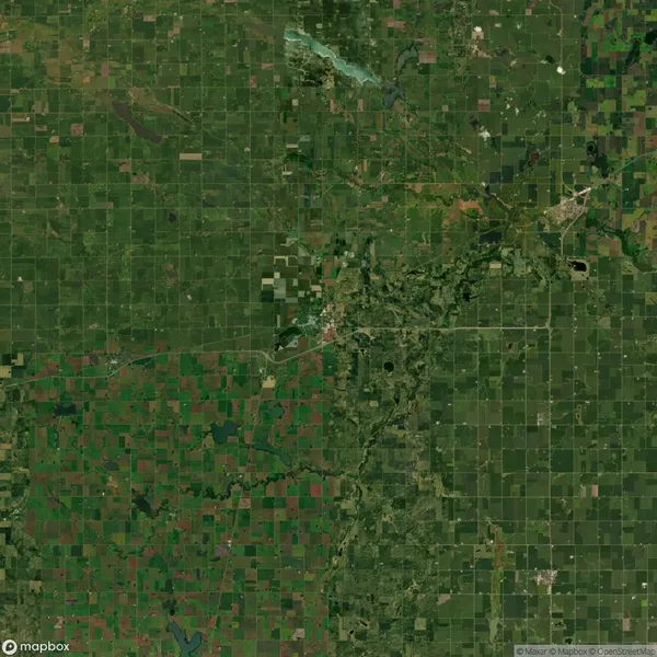 Satellite view of a rural landscape featuring a patchwork of agricultural fields, a river winding across the middle, and a small town center near the center-right of the image.
