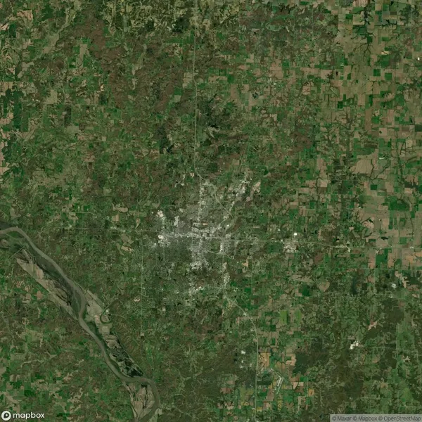 Satellite view of a city surrounded by rural and green areas, with a river visible in the bottom left corner.