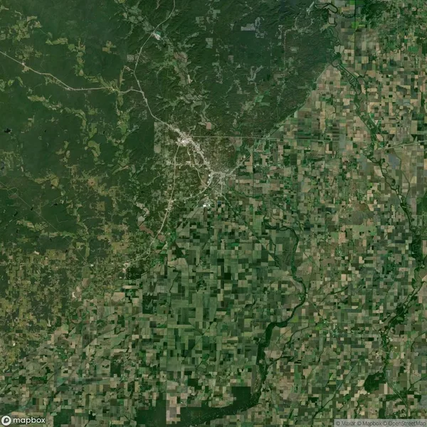 Aerial view of a landscape with a dense forest on the left, a city in the center, and agricultural fields on the right, all interspersed by roads.