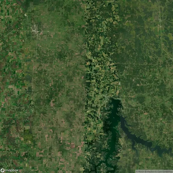 Aerial view of green landscapes divided by a darker, forested area with a river flowing through it, surrounded by rural and agricultural land.