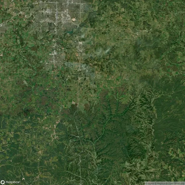 Aerial view of a landscape showing a mix of urban and rural areas with distinct green spaces, roads, and a river running through the bottom right section.