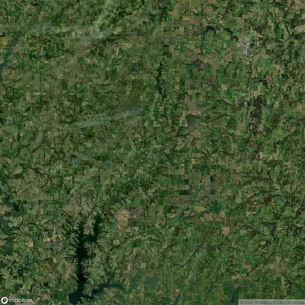 Aerial view of a rural landscape with green fields, forests, and a large lake in the bottom left corner.