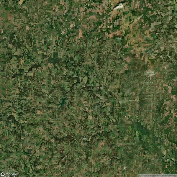 Aerial view of a rural landscape featuring a patchwork of fields, forests, and a winding river. Roads and small settlements are scattered throughout the greenery.