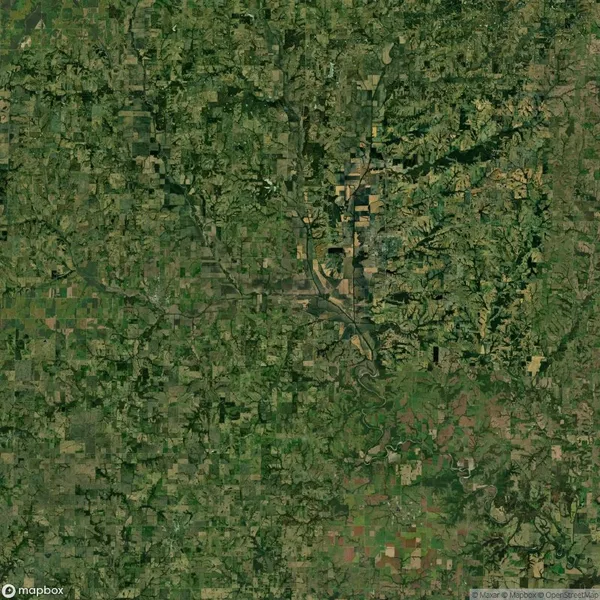 Aerial view of a landscape featuring a patchwork of agricultural fields, roads, and scattered wooded areas. A river meanders through the center, surrounded by diverse terrain.