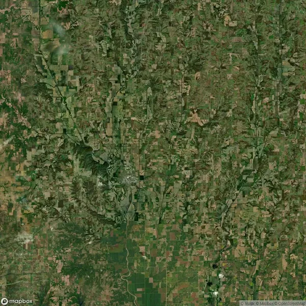 Aerial view of a patchwork landscape with fields, roads, and rivers interspersed with green areas. Terrain shows varied textures and tones, indicating different land uses and natural features.