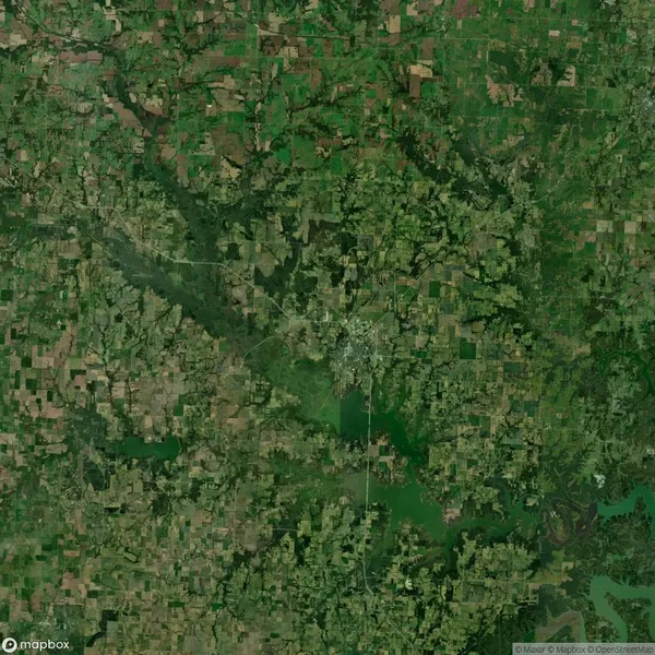 Aerial view of a landscape with a mix of green fields, forests, and patches of farmland. Roads and waterways are visible throughout the terrain.