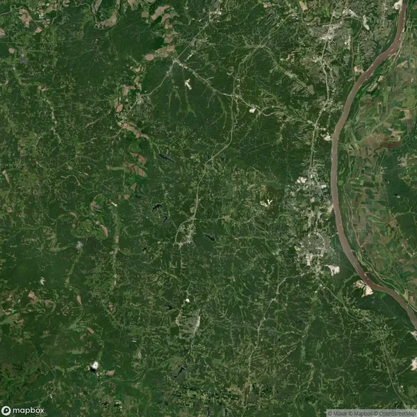 Aerial view of a green landscape with winding roads and sparse settlements near a river on the right.