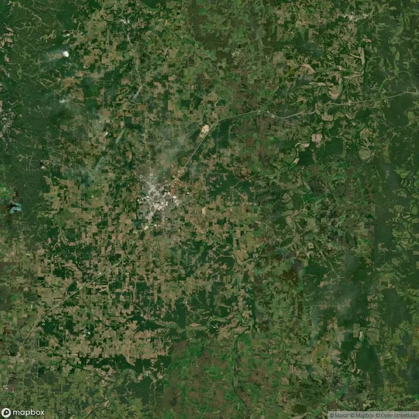 Aerial view of a densely populated urban area surrounded by green and brown agricultural fields. Roads and small water bodies are visible throughout the landscape.
