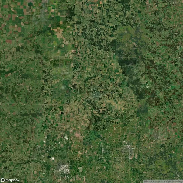 Aerial view of a rural landscape with a patchwork of green and brown fields, roads, and scattered trees.
