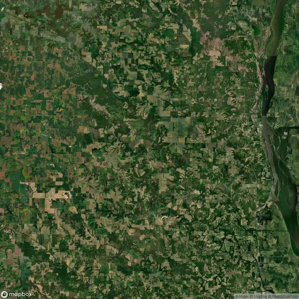 Aerial view of a landscape with a patchwork of agricultural fields and forests. A winding river is visible on the right side of the image.