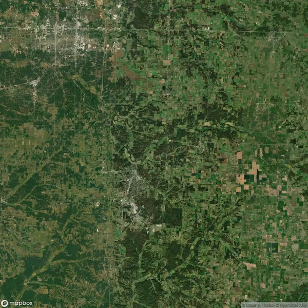 Aerial view of a landscape showing a blend of urban and rural areas with a patchwork of fields, forests, and roads.