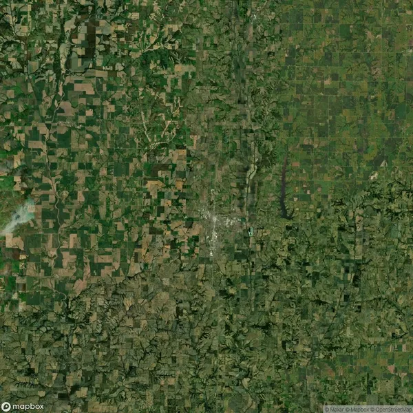 Aerial view of a rural landscape featuring a patchwork of agricultural fields and sparse tree cover. A small urban area is visible near the center.