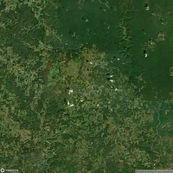 Satellite view of a largely green landscape with patches of farmland and forested areas, some clouds scattered across the image.