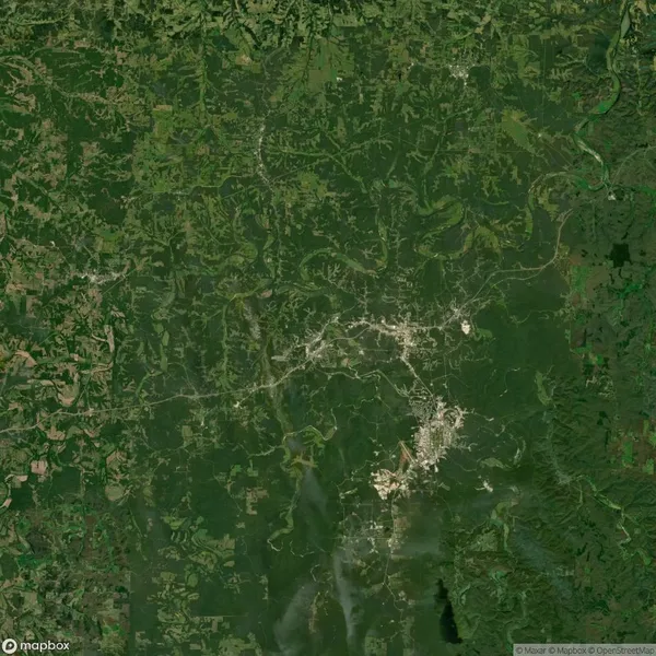 Aerial view of a densely forested area with winding roads and small clusters of buildings throughout, surrounded by patches of cleared land.