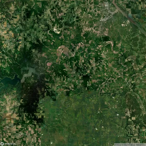 Aerial view of a green landscape with fields, forests, and a winding river. Patches of urban areas are visible in the upper right corner.