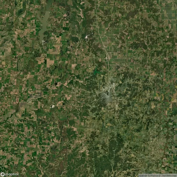 Aerial view of a rural landscape with patchwork fields, roads, and scattered trees, centered around a small urban area.