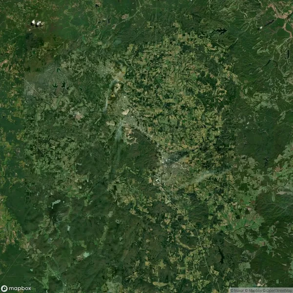 Aerial view of a densely vegetated landscape with scattered clearings, roads, and small water bodies.