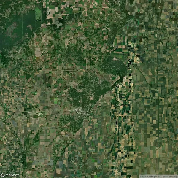 Aerial view of a patchwork landscape featuring fields, forests, and a river with a network of roads and urban areas.