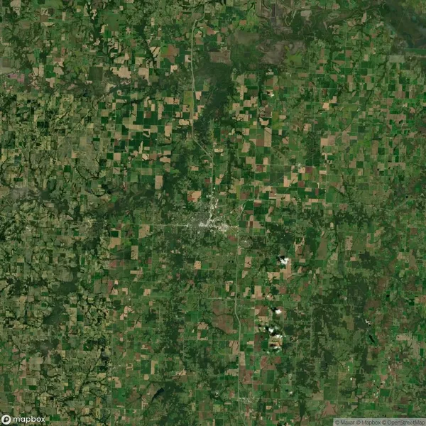 Satellite view of a rural area with a patchwork of green and brown agricultural fields surrounding a central small town.
