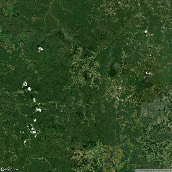 Aerial view of a lush green landscape with scattered clouds. Visible are fields, dense forests, and winding roads.