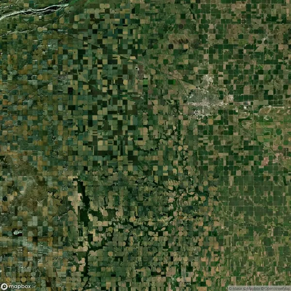 Aerial view of a patchwork landscape with a mix of square and circular agricultural fields; a small town is visible in the top right quadrant.