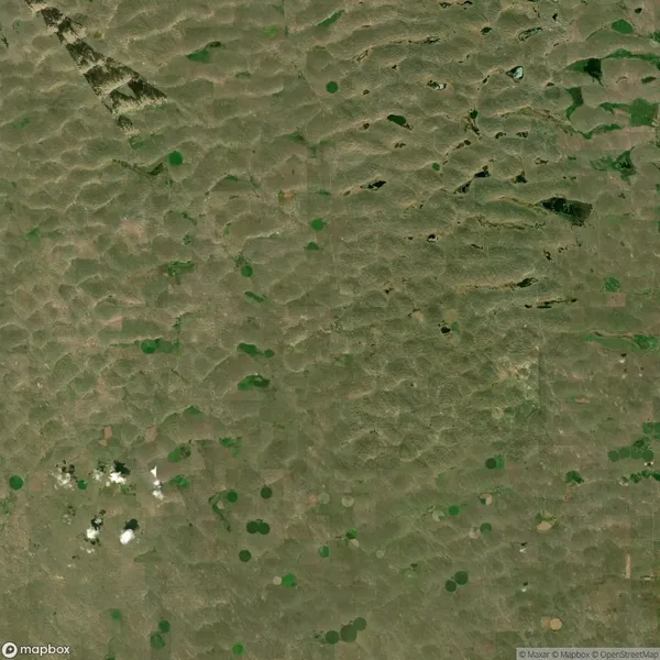 Aerial view of a rural landscape with scattered green circular fields and patches of trees, indicating agricultural activity amidst a largely brown terrain.