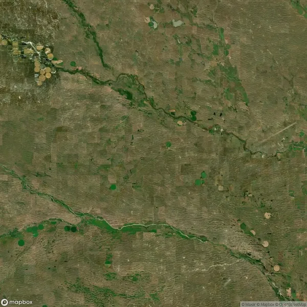 Aerial view of a rural landscape with patchy farmland, scattered circular fields, and winding rivers. Sparse vegetation and uniform terrain are visible.