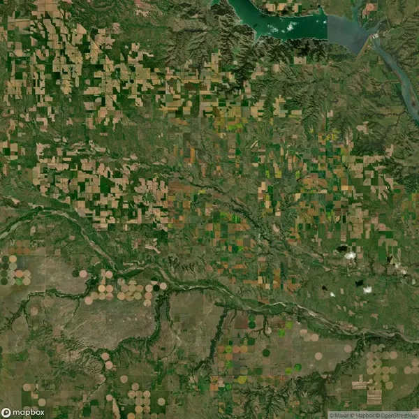 Aerial view of a landscape featuring a patchwork of rectangular and circular agricultural fields with a river cutting through, and a water body at the top of the image.