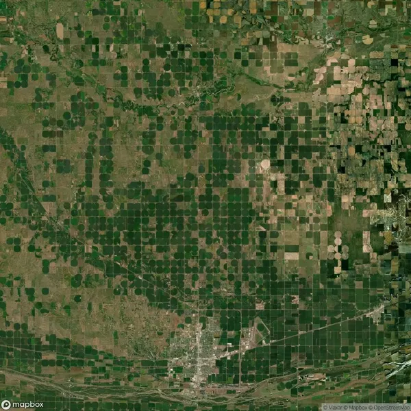 Aerial view of a landscape with green and brown patchwork fields, a pattern of circular and rectangular plots, and a small town at the bottom.