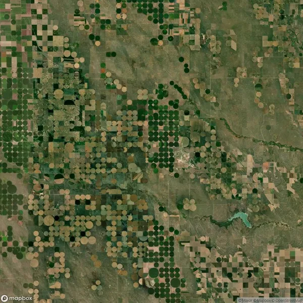 Aerial view of farmland with circular and rectangular plots in shades of green and brown, showing crop patterns and irrigation systems.