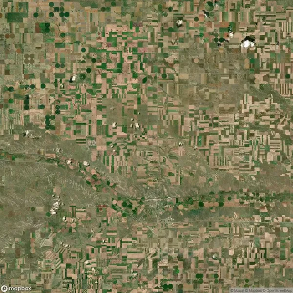 Aerial view of a patchwork landscape with circular and rectangular agricultural fields, intersected by a winding river and small clouds casting shadows.