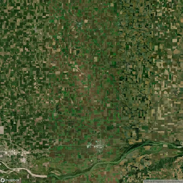 Aerial view of a vast agricultural landscape with a patchwork of rectangular farm fields, intersected by a river flowing through the lower part of the image.
