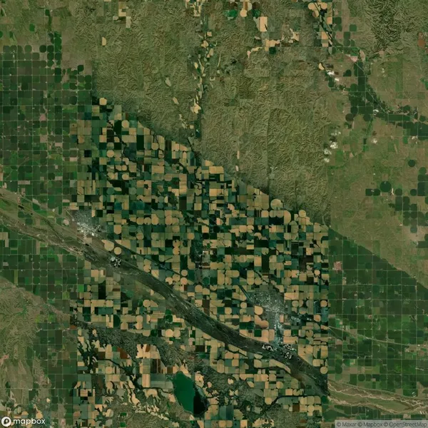 Aerial view of an agricultural landscape with circular and rectangular fields in varying shades of green and brown, intersected by roads and natural formations.