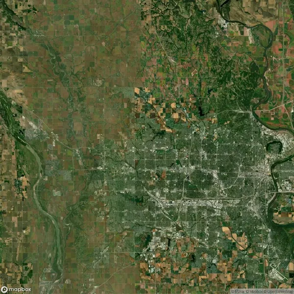 Aerial view of a large city with a dense grid of streets surrounded by agricultural fields and patches of greenery.