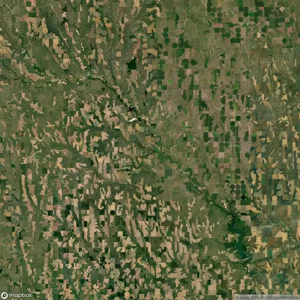 Satellite image of a rural landscape showing patchwork of agricultural fields, with varying shades of green and brown, intersected by a winding river or stream.