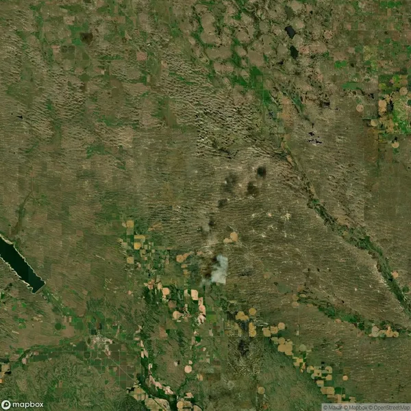 Satellite image showing a landscape with fields and patches of green and brown. A cluster of dark and light spots is visible near the center, possibly indicating vegetation or land features.