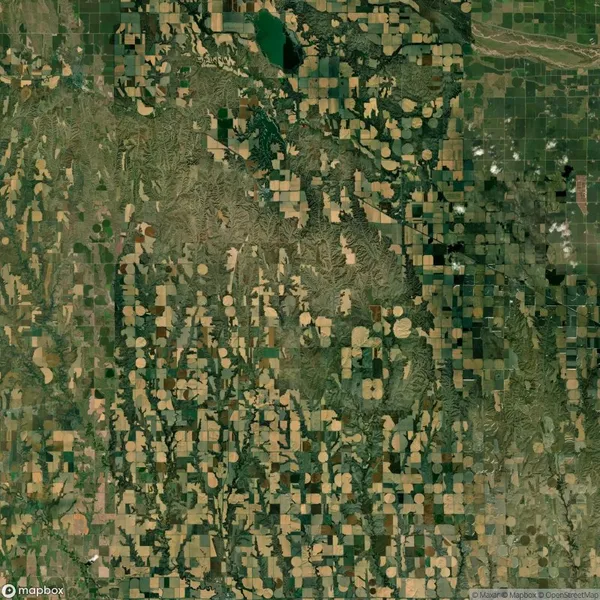 Aerial view of farmland with circular and rectangular plots. The landscape shows patterns of irrigation fields, roads, and patches of natural terrain.