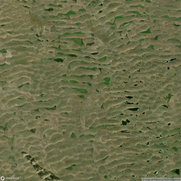 Aerial view of a landscape with irregular green patches and scattered small bodies of water on a rugged terrain.