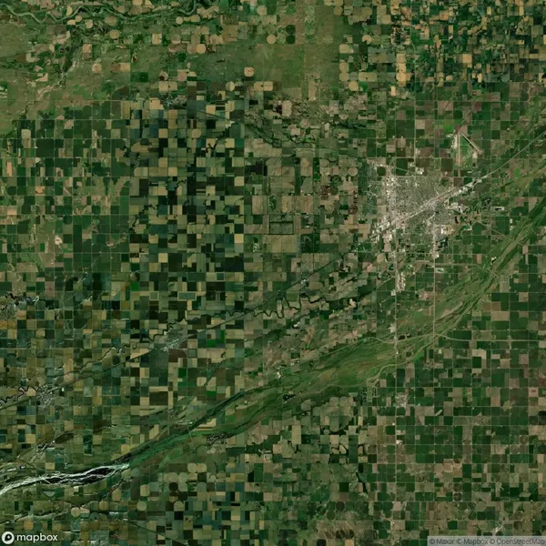 Aerial view of a patterned landscape featuring a patchwork of agricultural fields and a small urban area. Roads and a river run through the region.