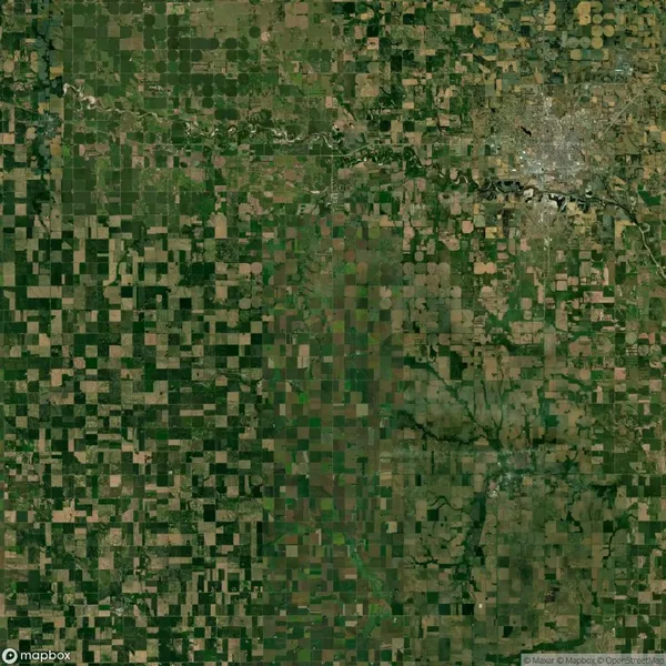Aerial view of a patchwork landscape with agricultural fields and a densely developed urban area in the upper right corner.