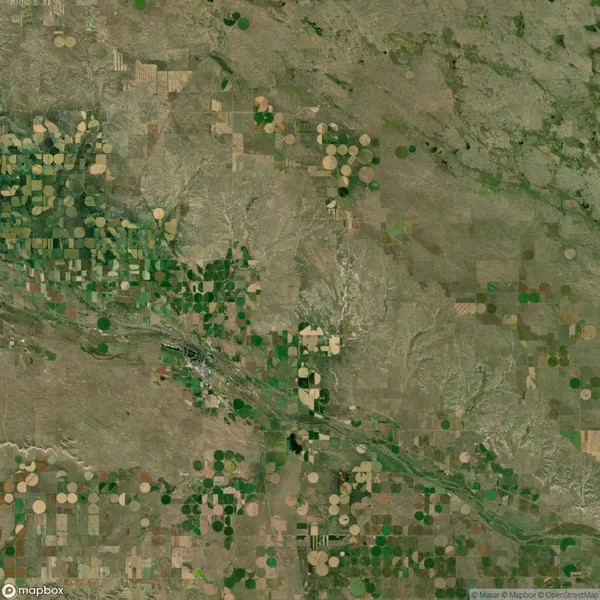 Aerial view of a landscape with a mix of square and circular agricultural fields in varying shades of green and brown, intersected by a river.