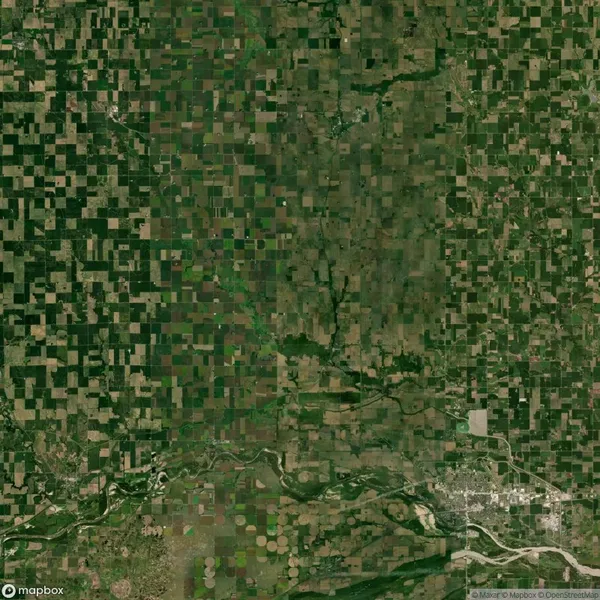 Aerial view of a large patchwork of agricultural fields with a river flowing across the bottom and a town in the lower right corner.