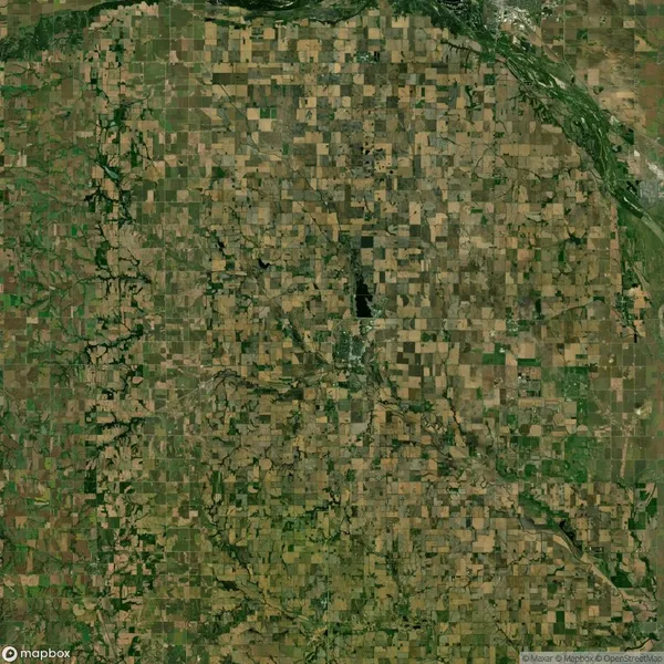 Aerial view of a large patchwork of agricultural fields with varying shades of green and brown, intersected by roads, and a river on the upper edge.