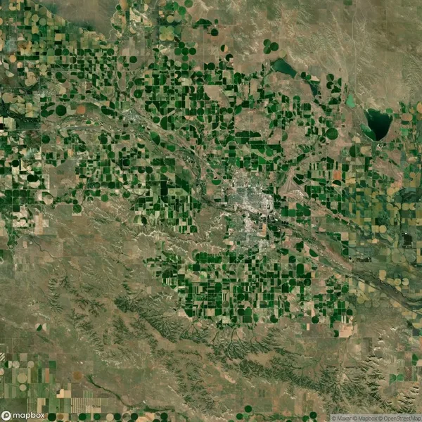 Aerial view of a landscape with green and brown agricultural fields and a small city at the center, surrounded by a semi-arid environment.