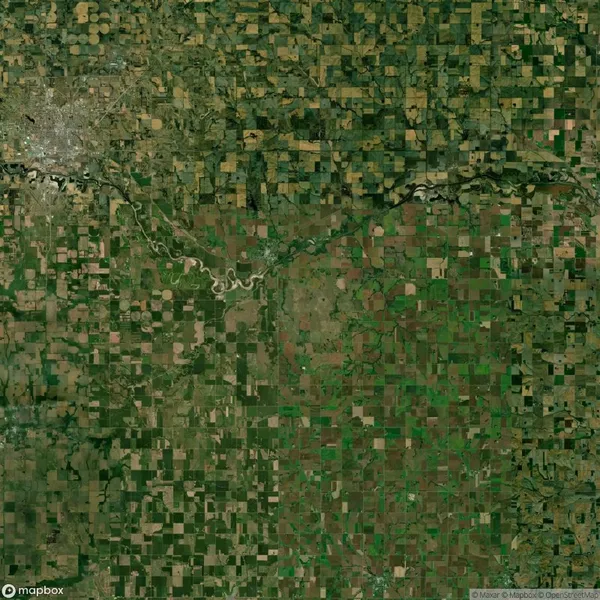 Aerial view of a patchwork of green and brown agricultural fields with a river running through and a city in the top left corner.