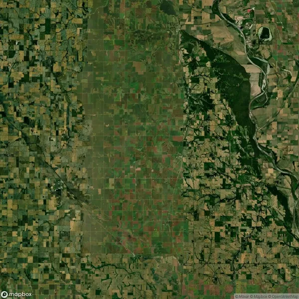 Aerial view of a patchwork landscape featuring agricultural fields and greenery. A river curves through the right side, bordered by a mix of wooded areas and more fields.